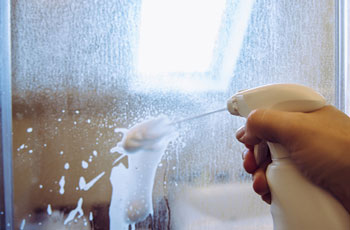 Person Sprays Cleaner on Shower Door