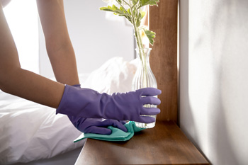 Cleaner Wearing Gloves Dusts Bedside Table with Microfiber Cloth